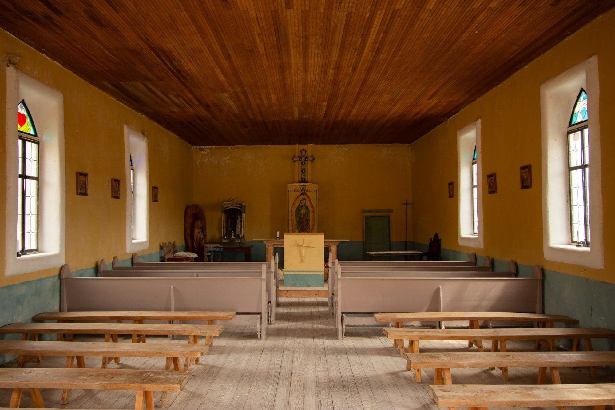 Simple sanctuary with wooden pews, a timber ceiling and stained glass windows